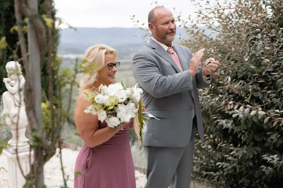 A woman holding white flowers and a man in grey applauding as the ceremony ends