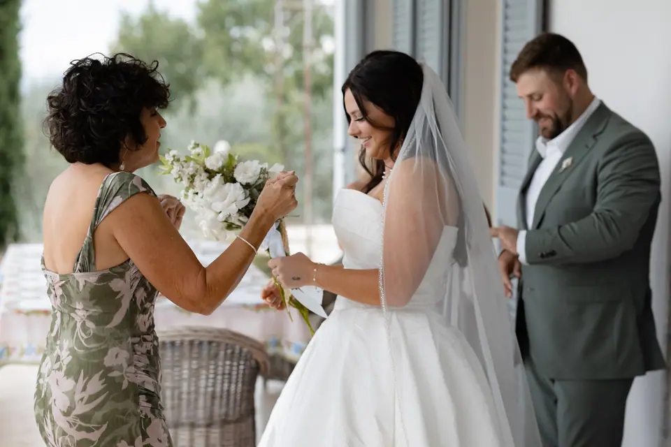 A guest in a floral dress pinning white flowers on Haley as Zach smiles beside her