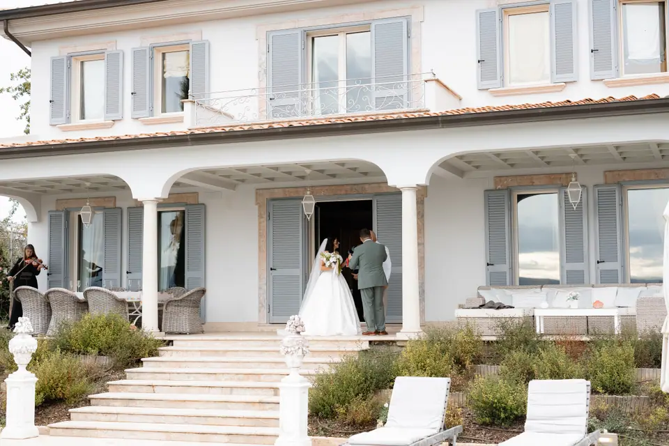 Haley and Zach stepping out of the white villa with blue shutters above the garden steps