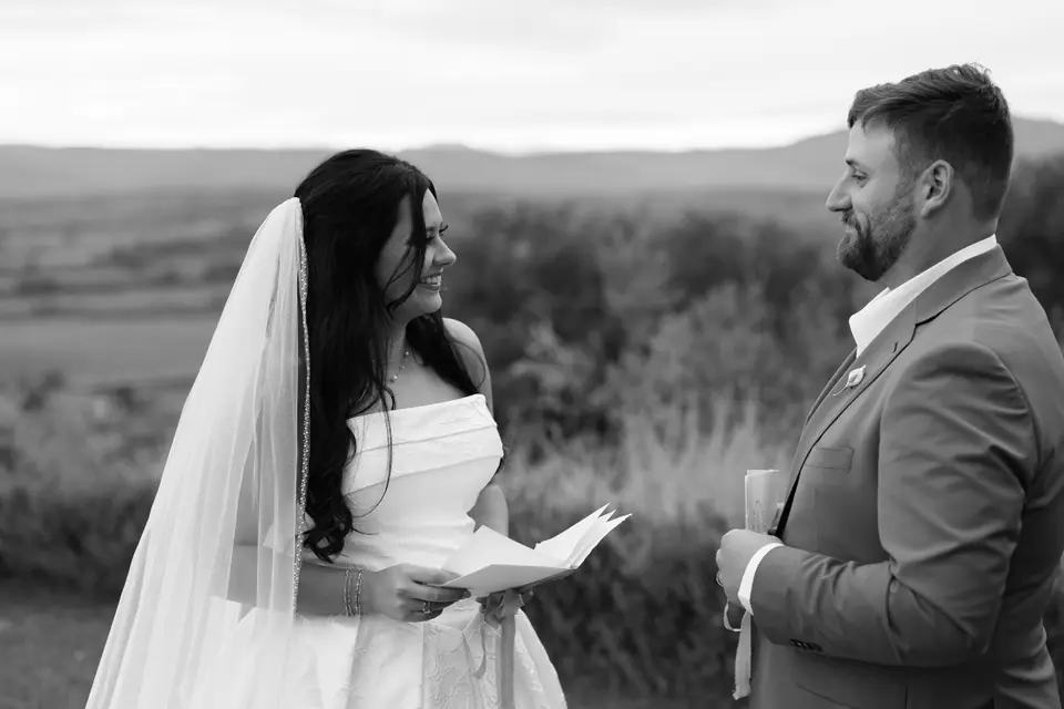 Black and white photograph of Haley and Zach reading their vows to each other above the hills