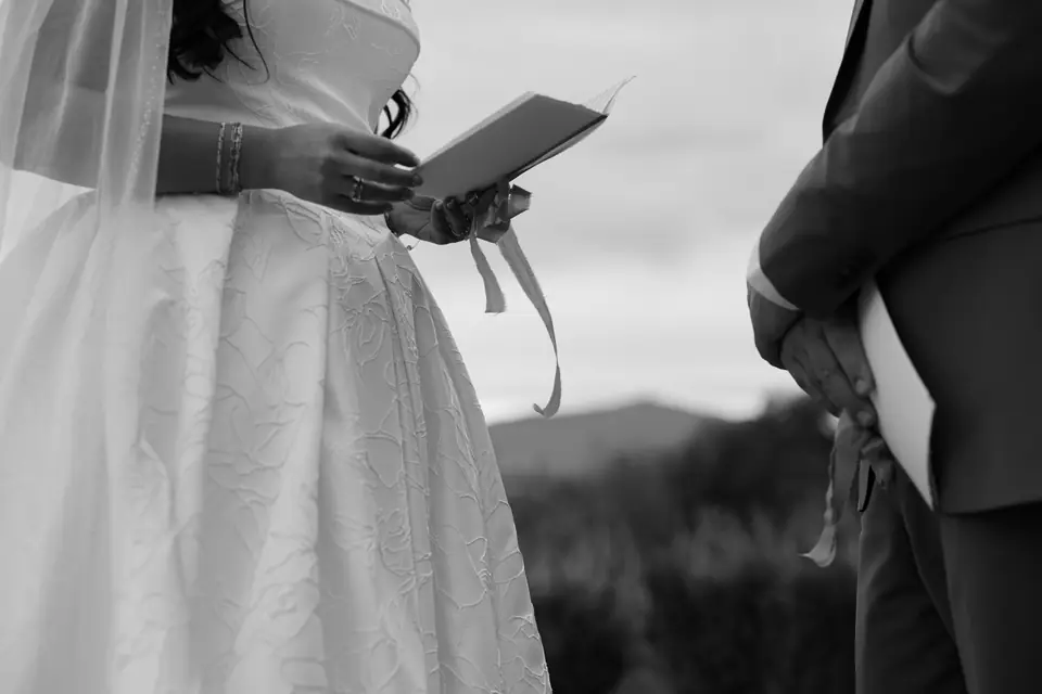 Black and white close-up of Haley holding her vow book as Zach stands beside her