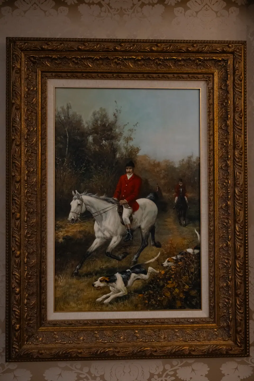 A gilt-framed painting of a rider on a white horse with hounds