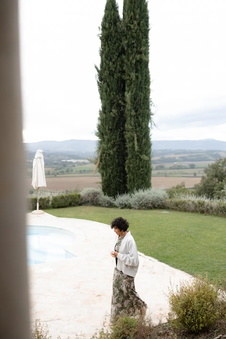 A guest in a floral skirt walking past the pool towards a tall cypress