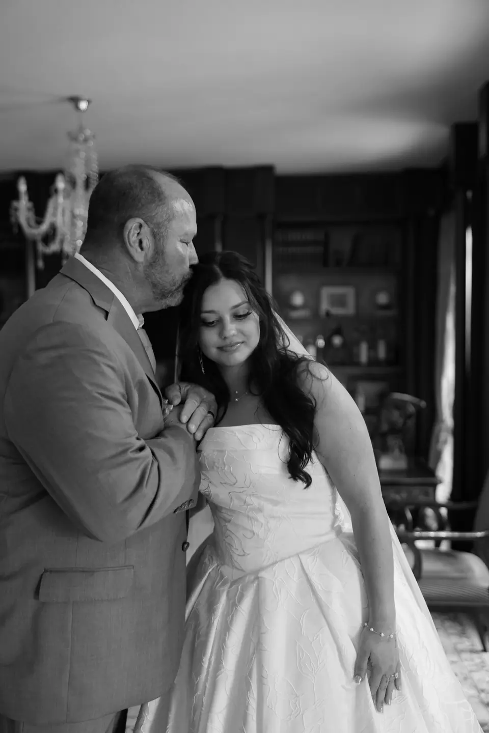 Black and white photograph of a man in a grey suit resting his cheek on Haley’s head