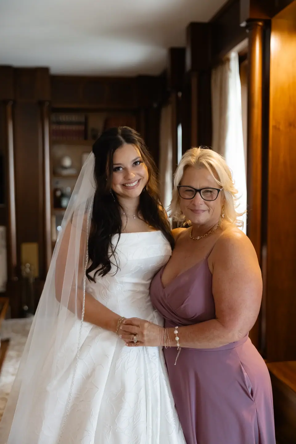 Haley in her veil smiling arm in arm with a woman in a mauve dress and glasses
