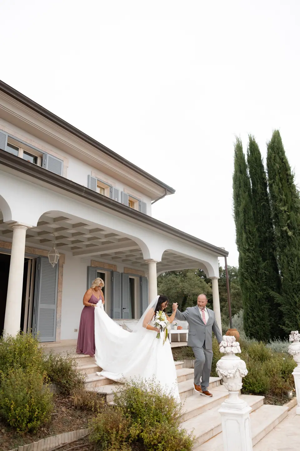 Haley stepping out of the villa with her train lifted, a man in grey beside her
