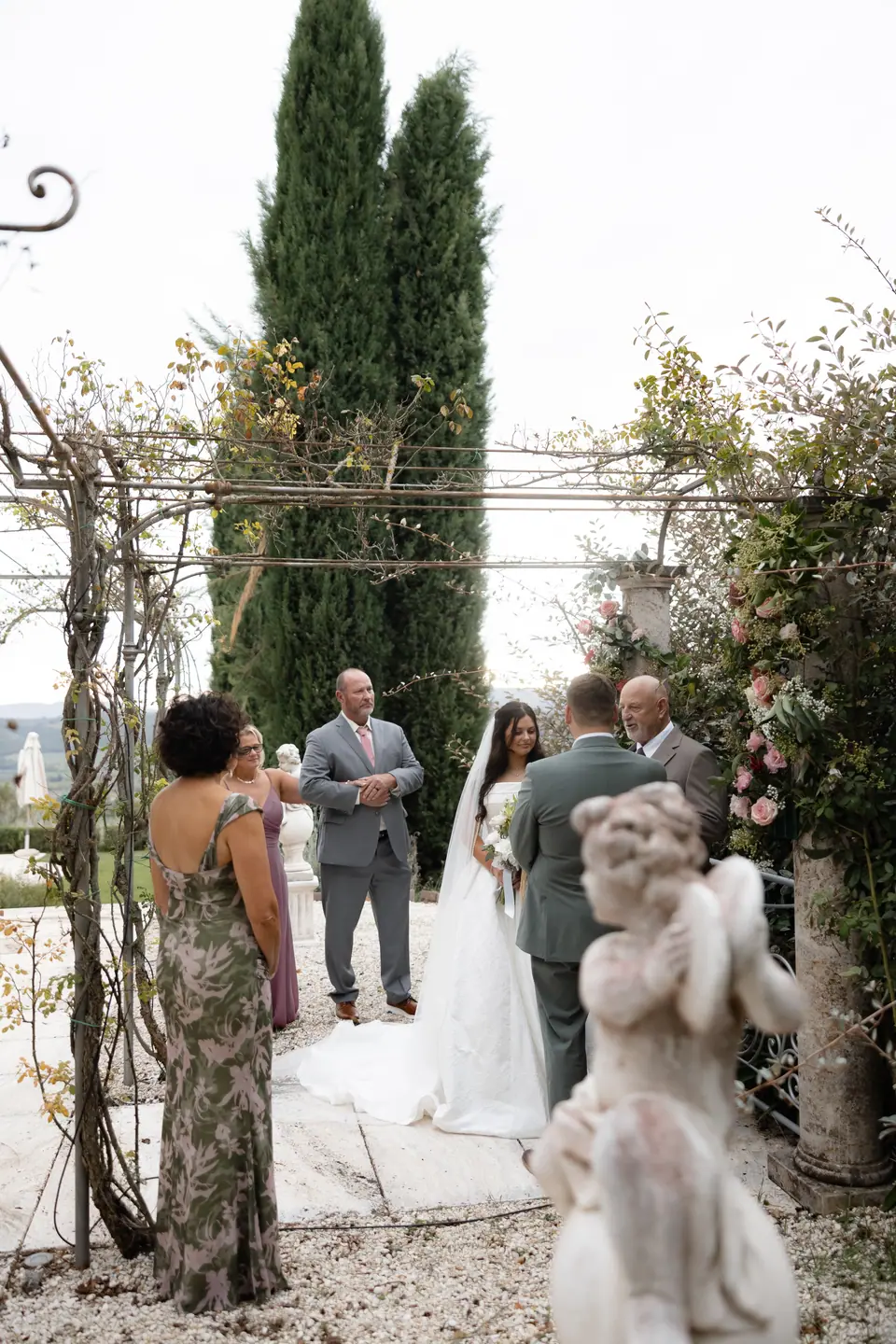 The ceremony beneath the pergola, seen past a stone cherub statue
