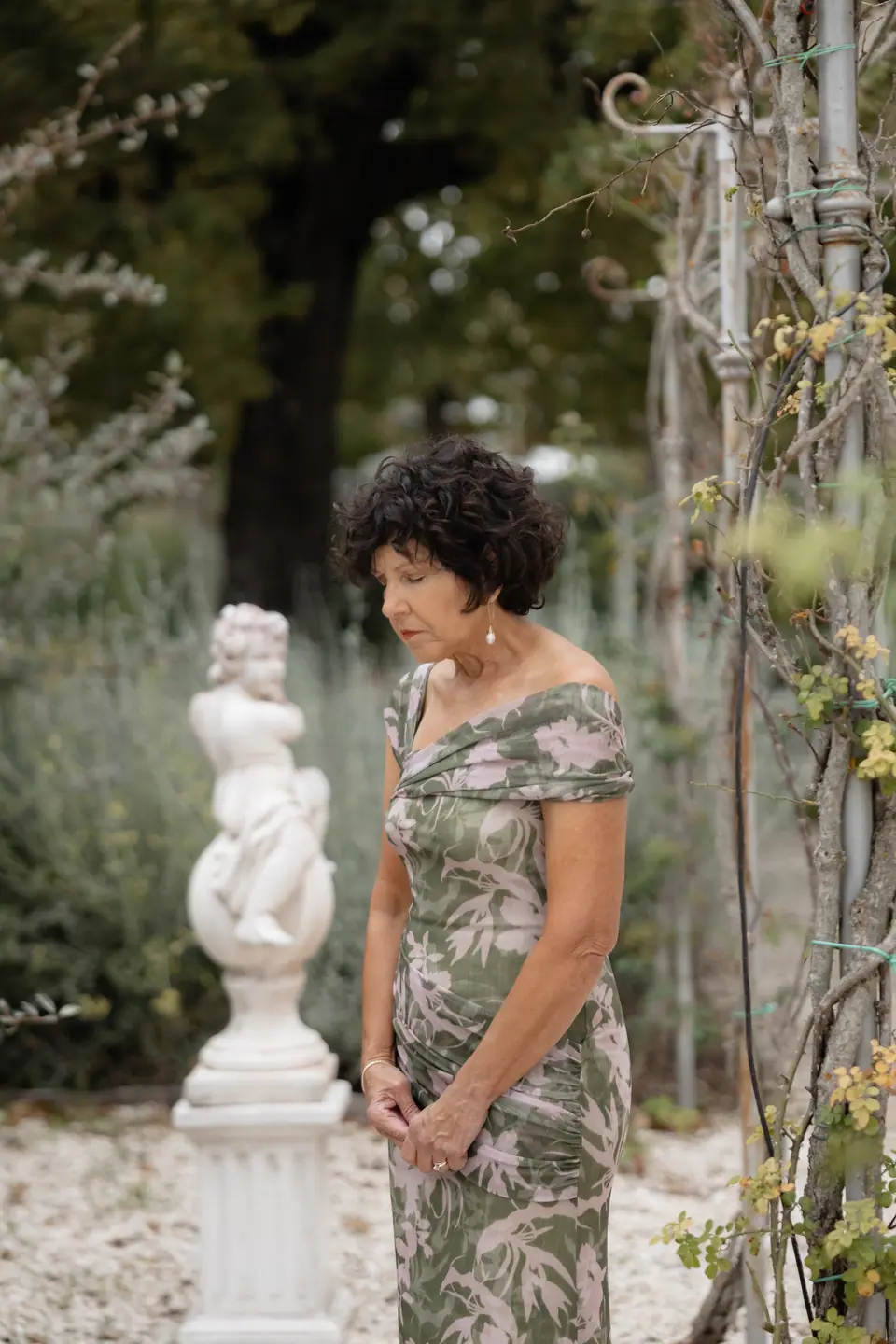 A woman in a floral dress beside a cherub statue, hands clasped during the ceremony