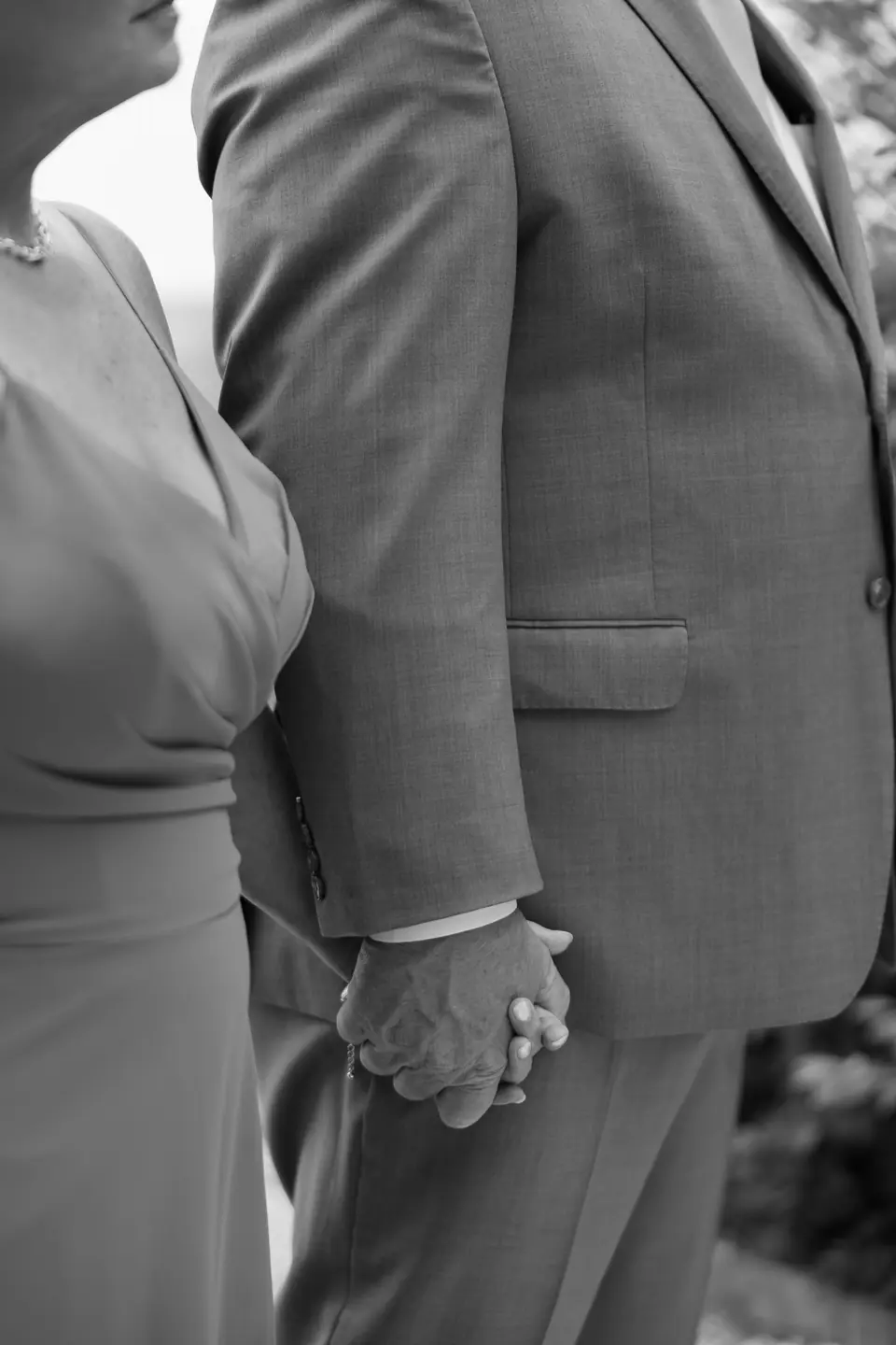 Black and white close-up of two guests holding hands as they watch the ceremony
