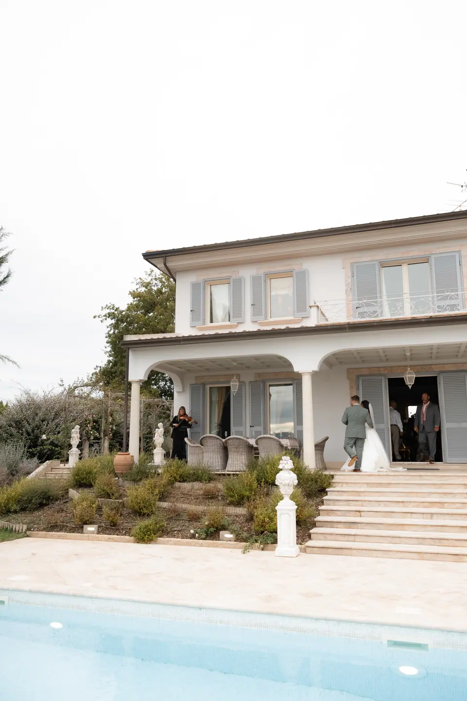 The white villa with blue shutters seen across the pool, the couple at the door
