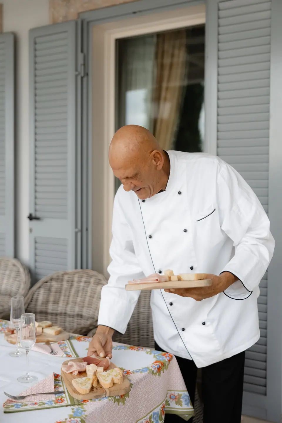 A chef in whites serving bread and cured meats at the terrace table