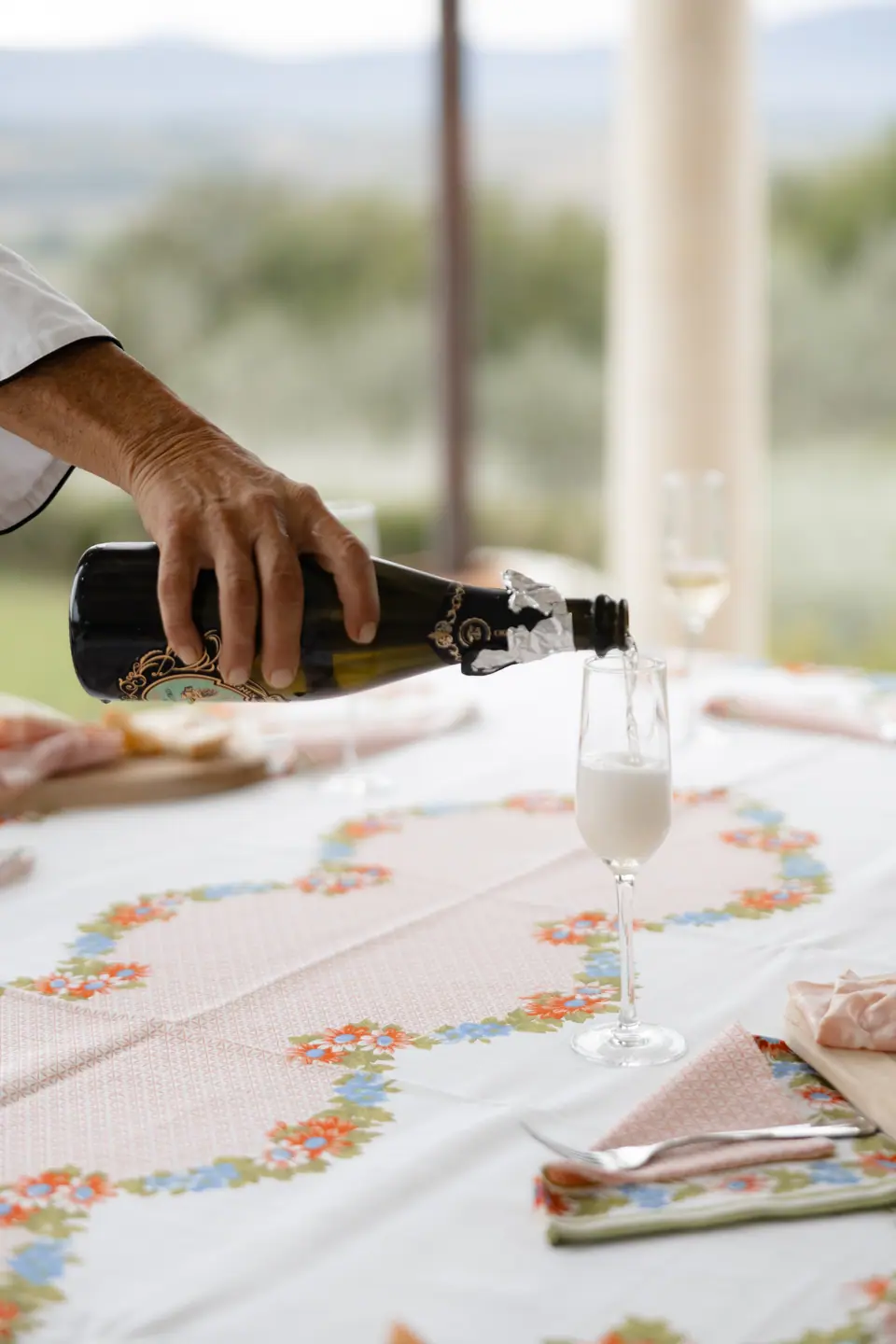 Prosecco poured into a glass on a floral tablecloth, the hills blurred behind