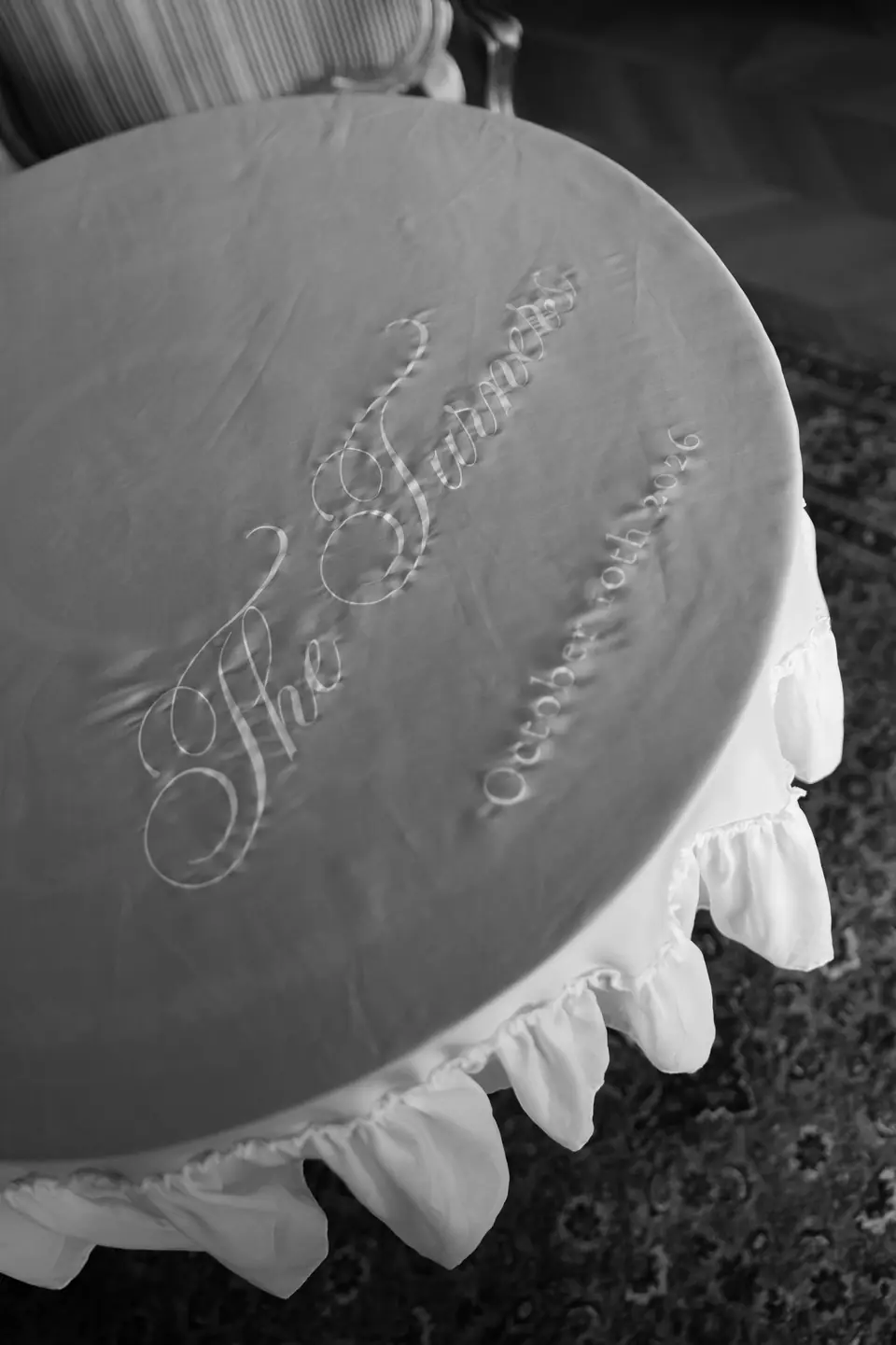 Black and white close-up of a round ruffled tablecloth embroidered in script