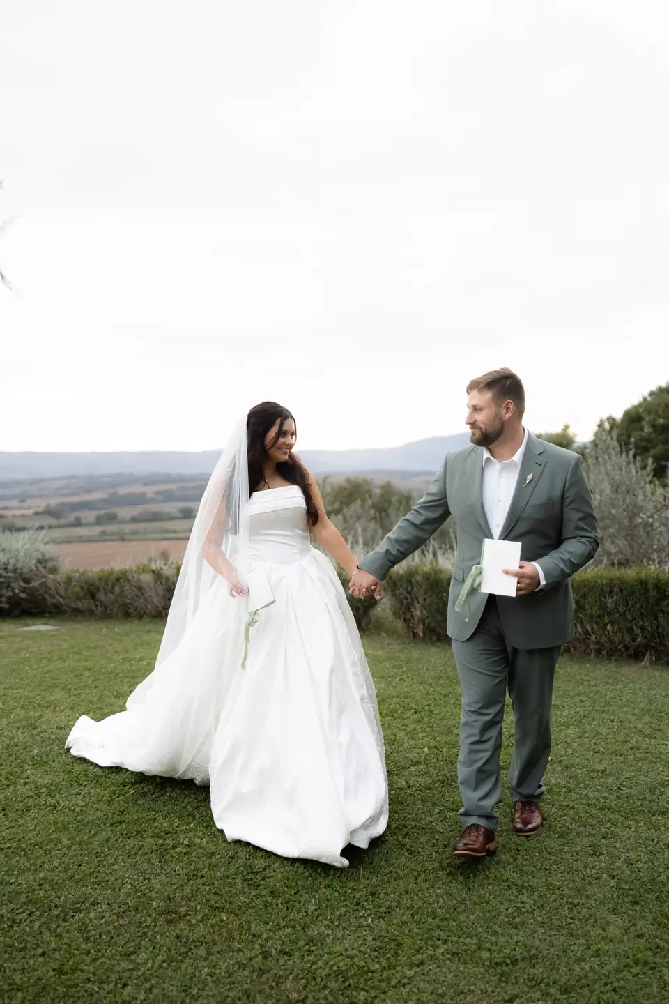 Haley and Zach walking hand in hand across the garden, with the Umbrian hills behind