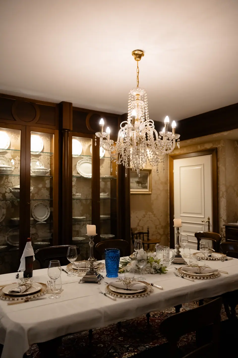 The candlelit dining room set for dinner under a crystal chandelier