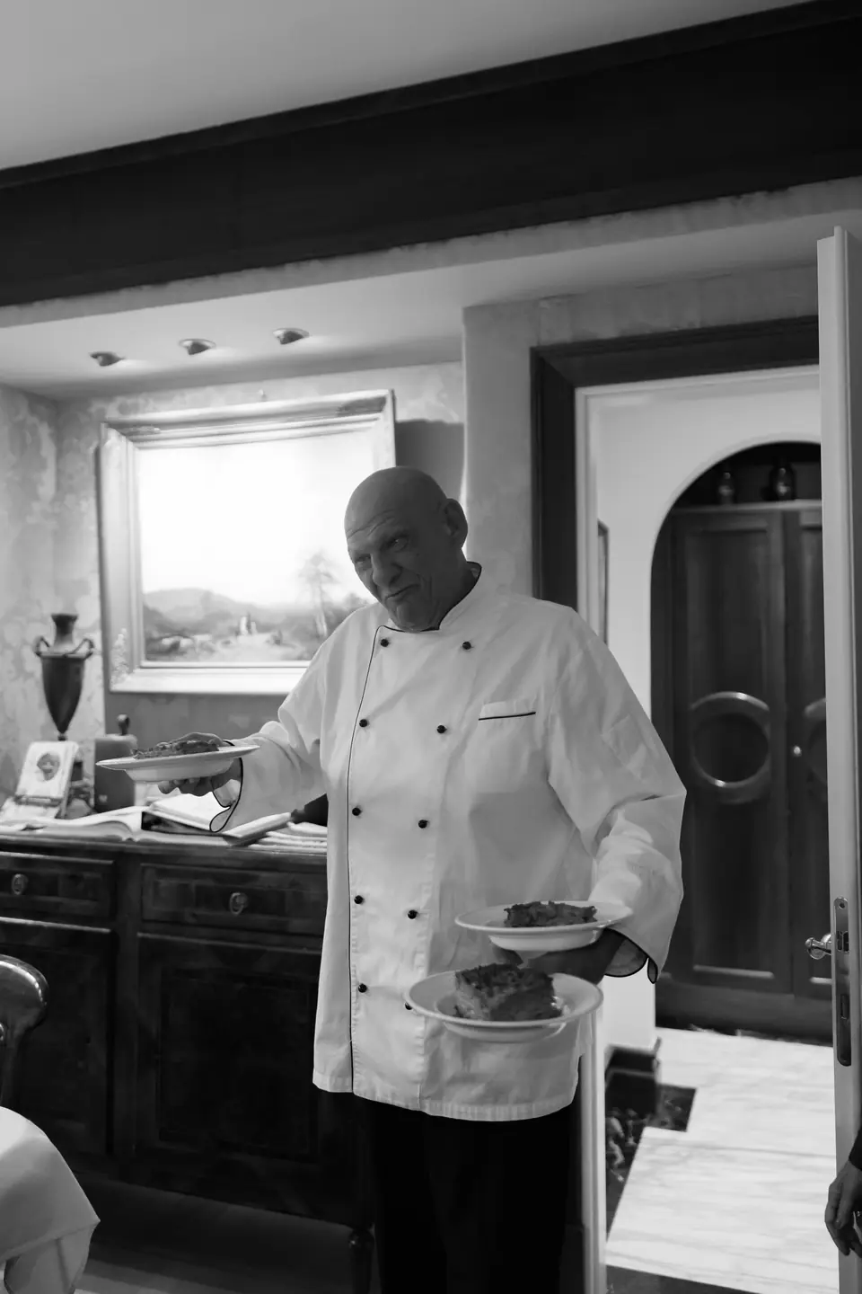 Black and white photograph of the chef carrying plates into the dining room