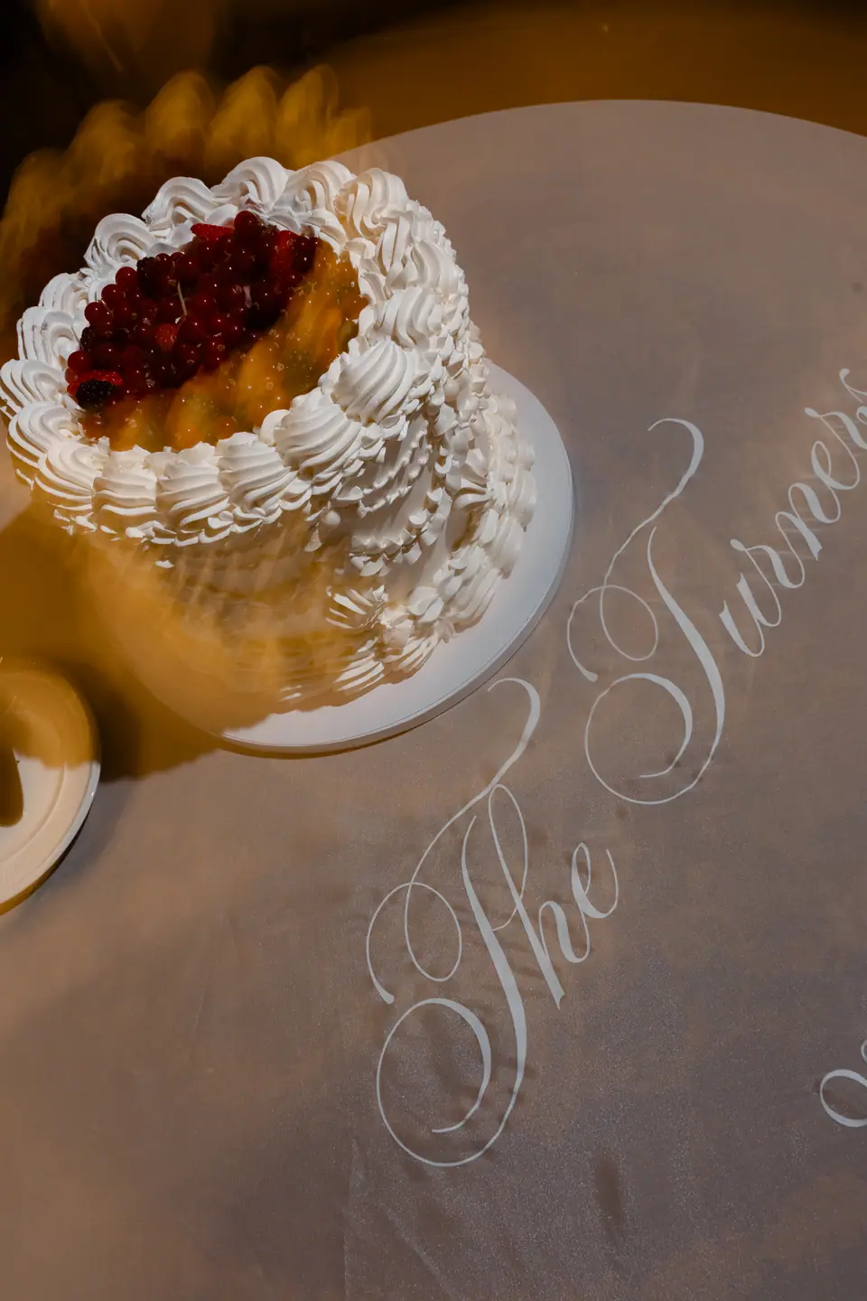 A cake topped with red berries on a cloth embroidered “The Turners”