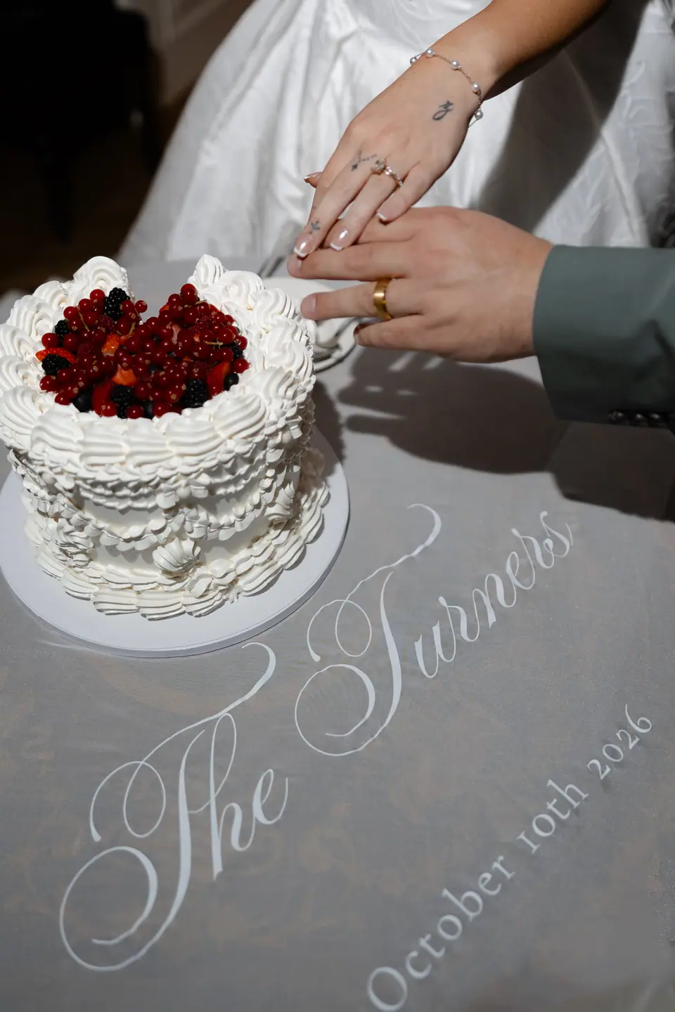 Their hands on the cake knife, the cloth embroidered “The Turners, October 10th 2026”