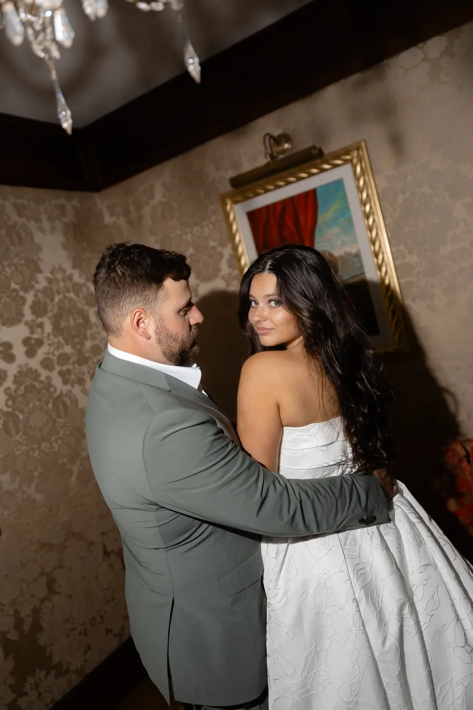 Zach holding Haley as she looks back over her shoulder against damask walls