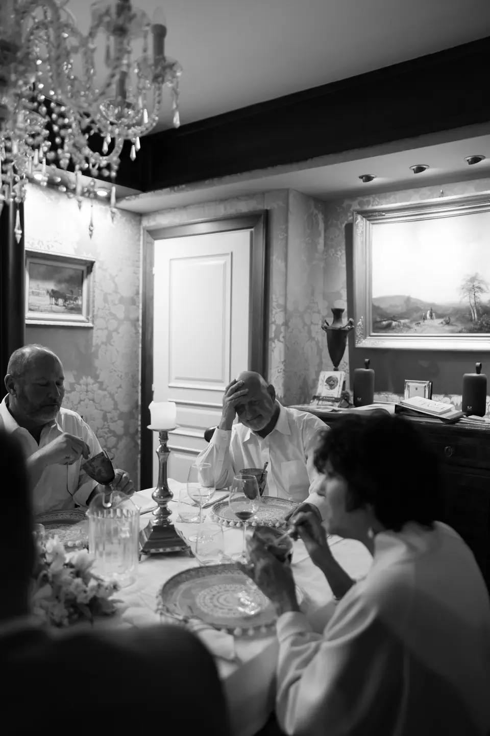 Black and white photograph of guests talking at dinner under the chandelier