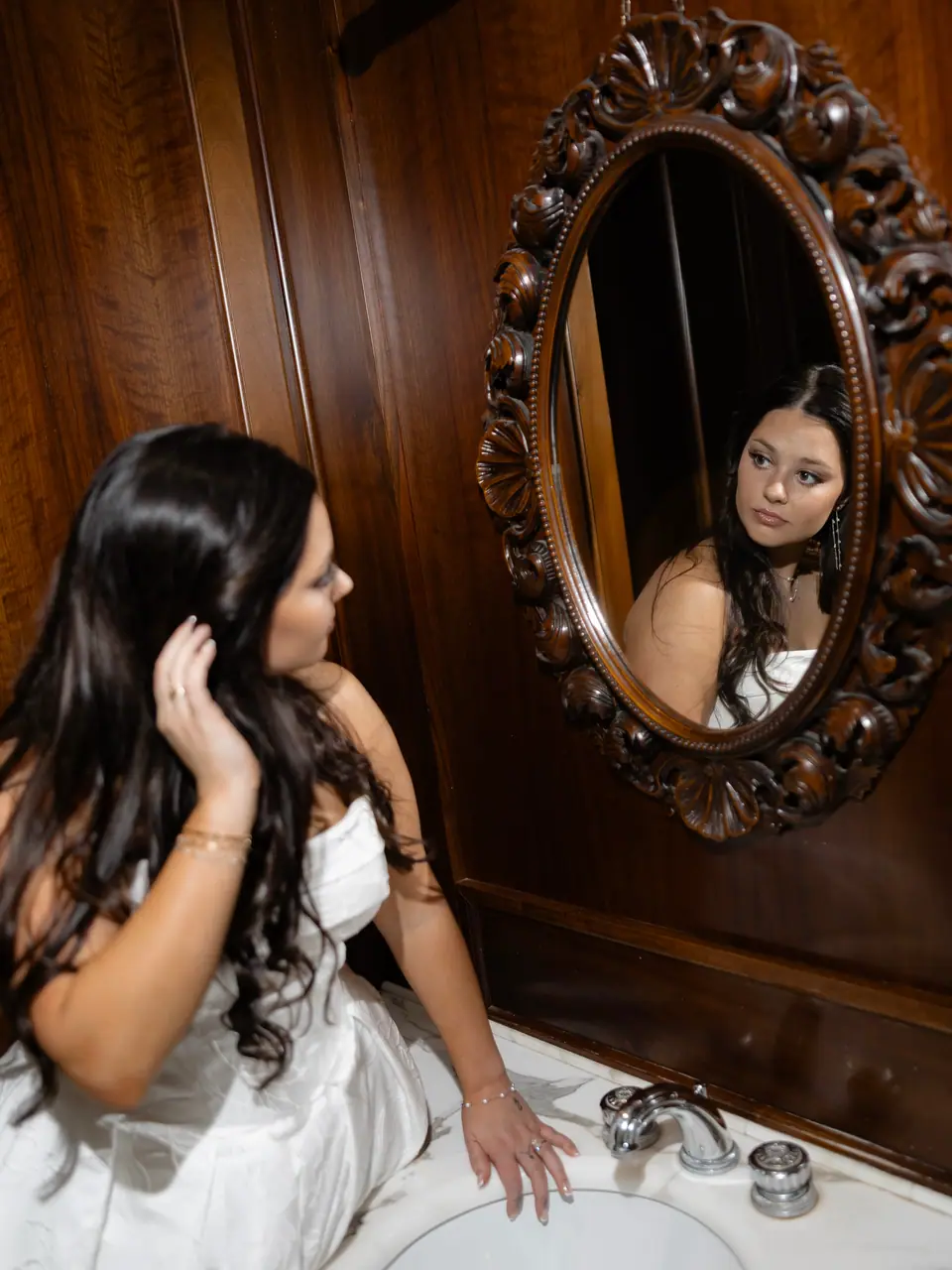Haley touching her hair before the carved oval mirror in the wood-panelled bathroom