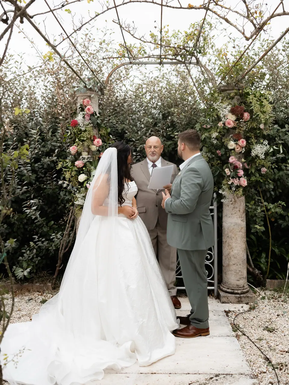Haley and Zach facing the officiant under a rose-covered arch