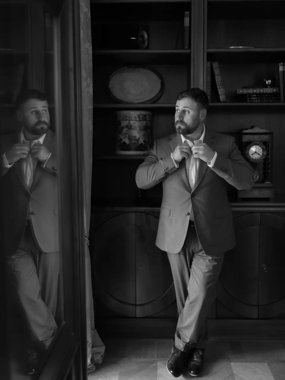 Black and white photograph of Zach fixing his cuffs beside his reflection in a dark cabinet