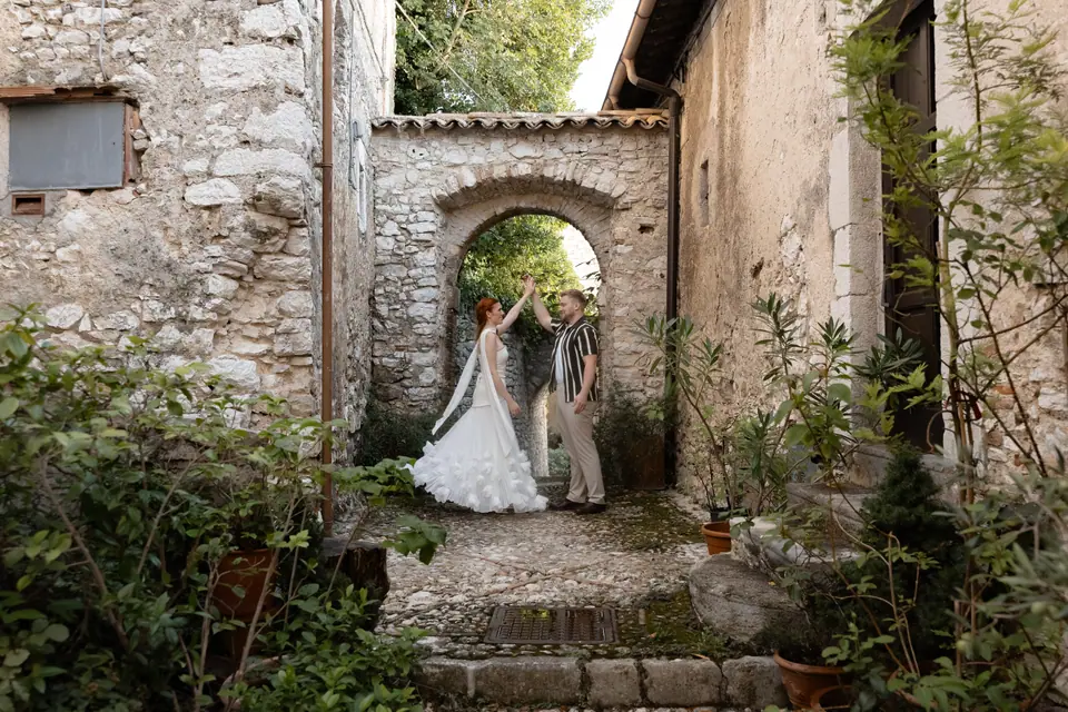 Kate and James dancing in a stone alley beneath an arch, framed by plants