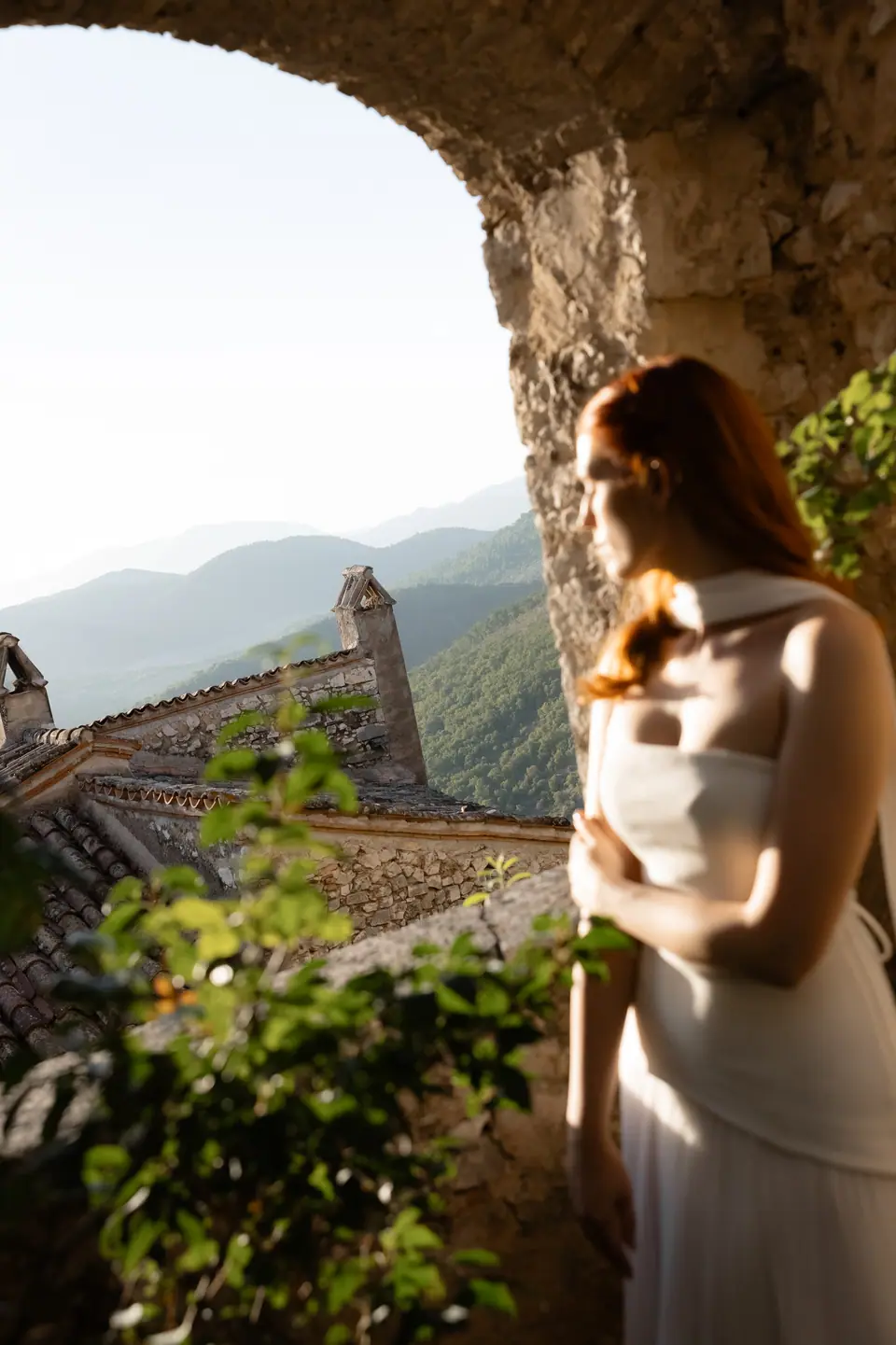 Kate in a cream dress looking out through a stone arch toward the mountains