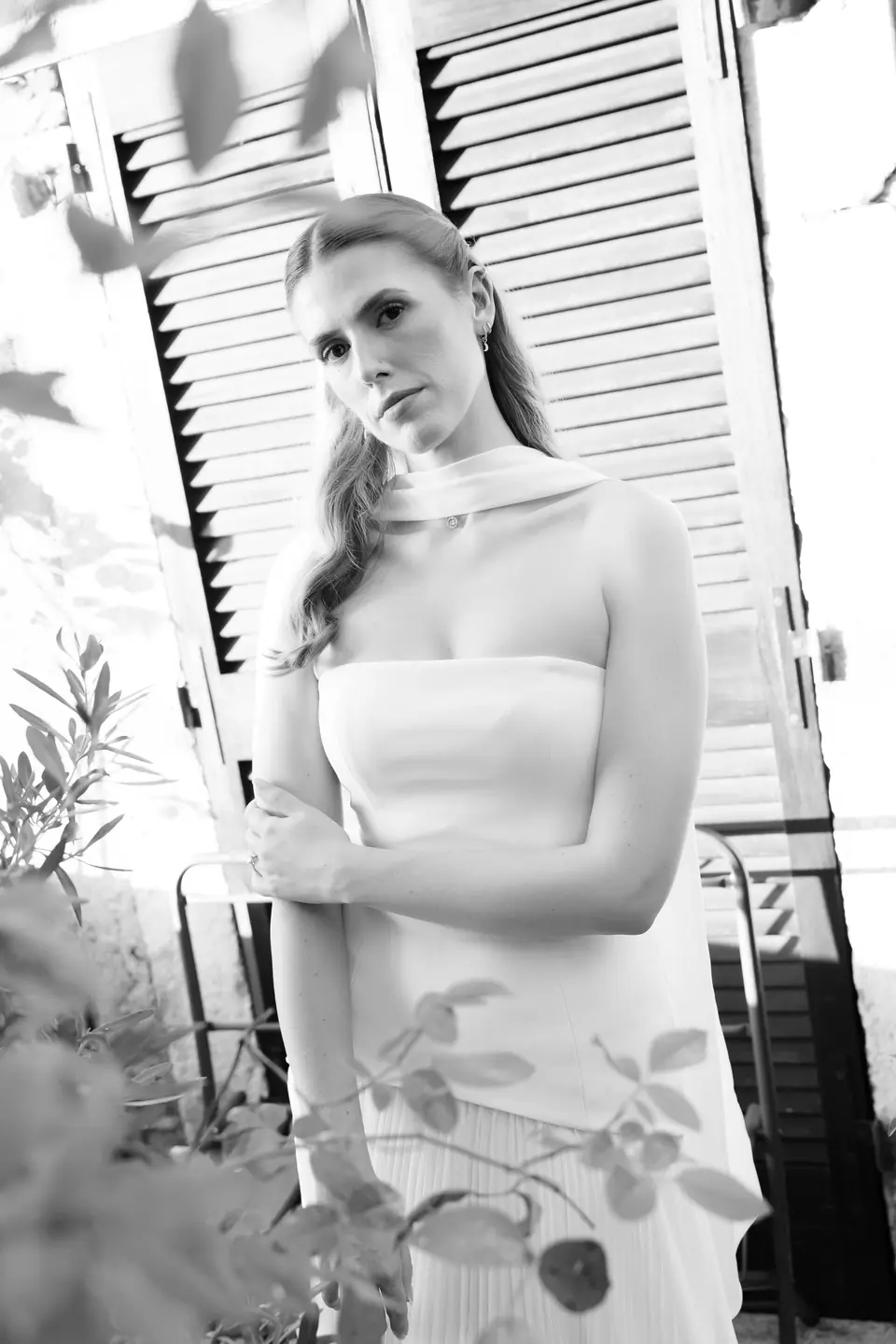 Black and white portrait of Kate in front of white shutters, a scarf around her neck