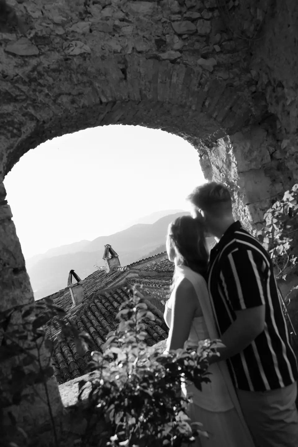 A black and white photograph of Kate and James beneath a stone archway overlooking the valley
