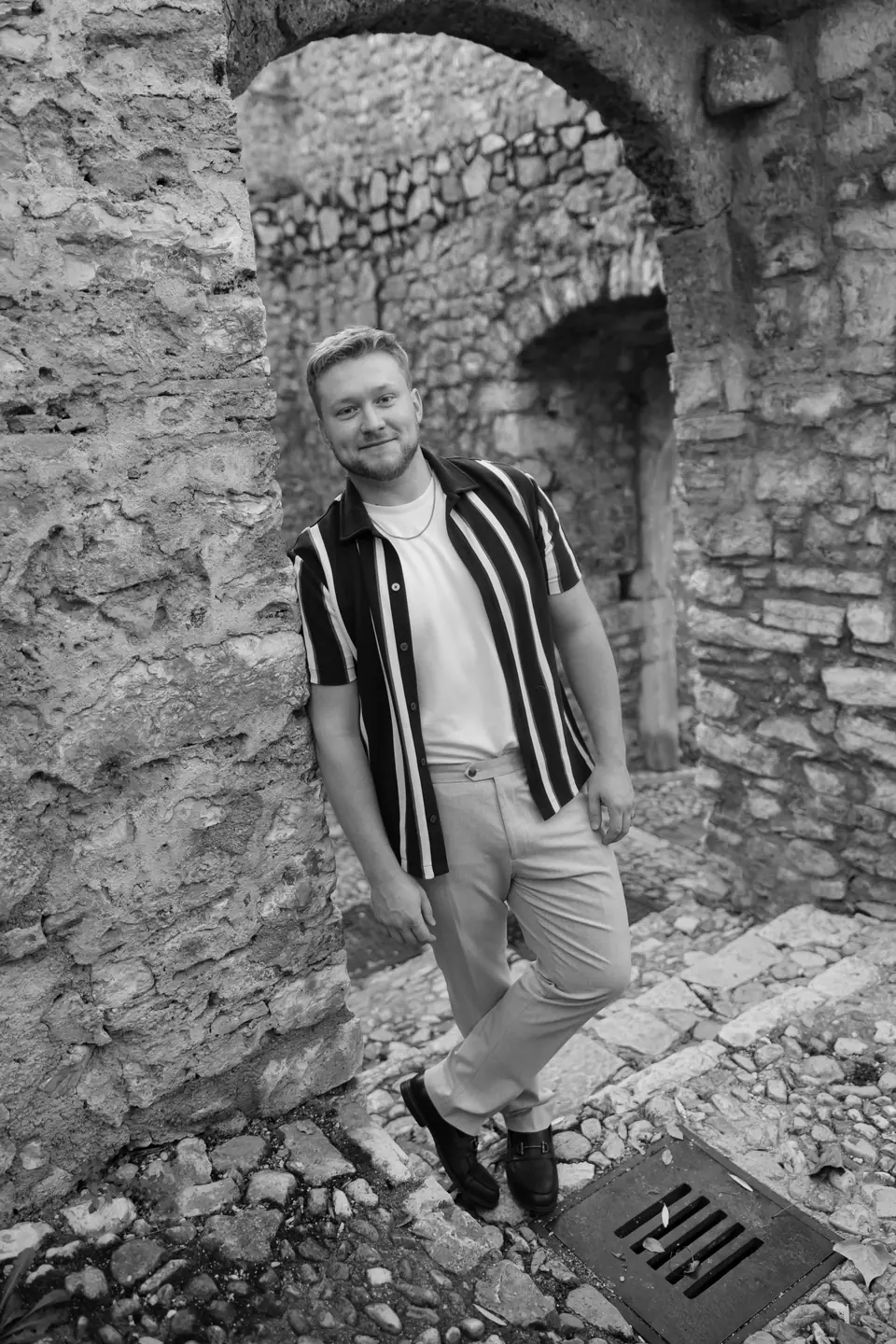 James in black and white leaning against a stone archway