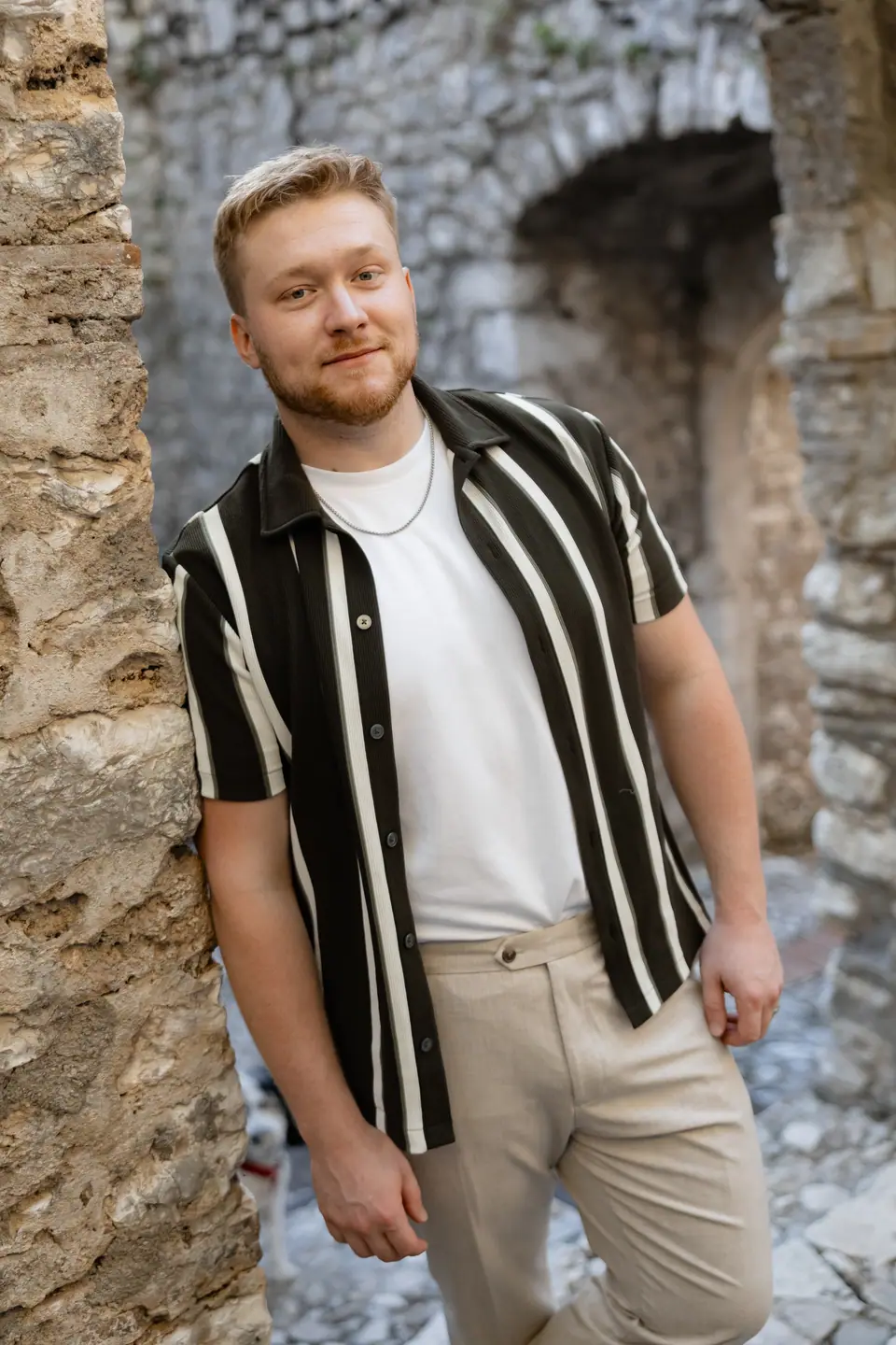 James in a striped shirt smiling beside a weathered stone wall