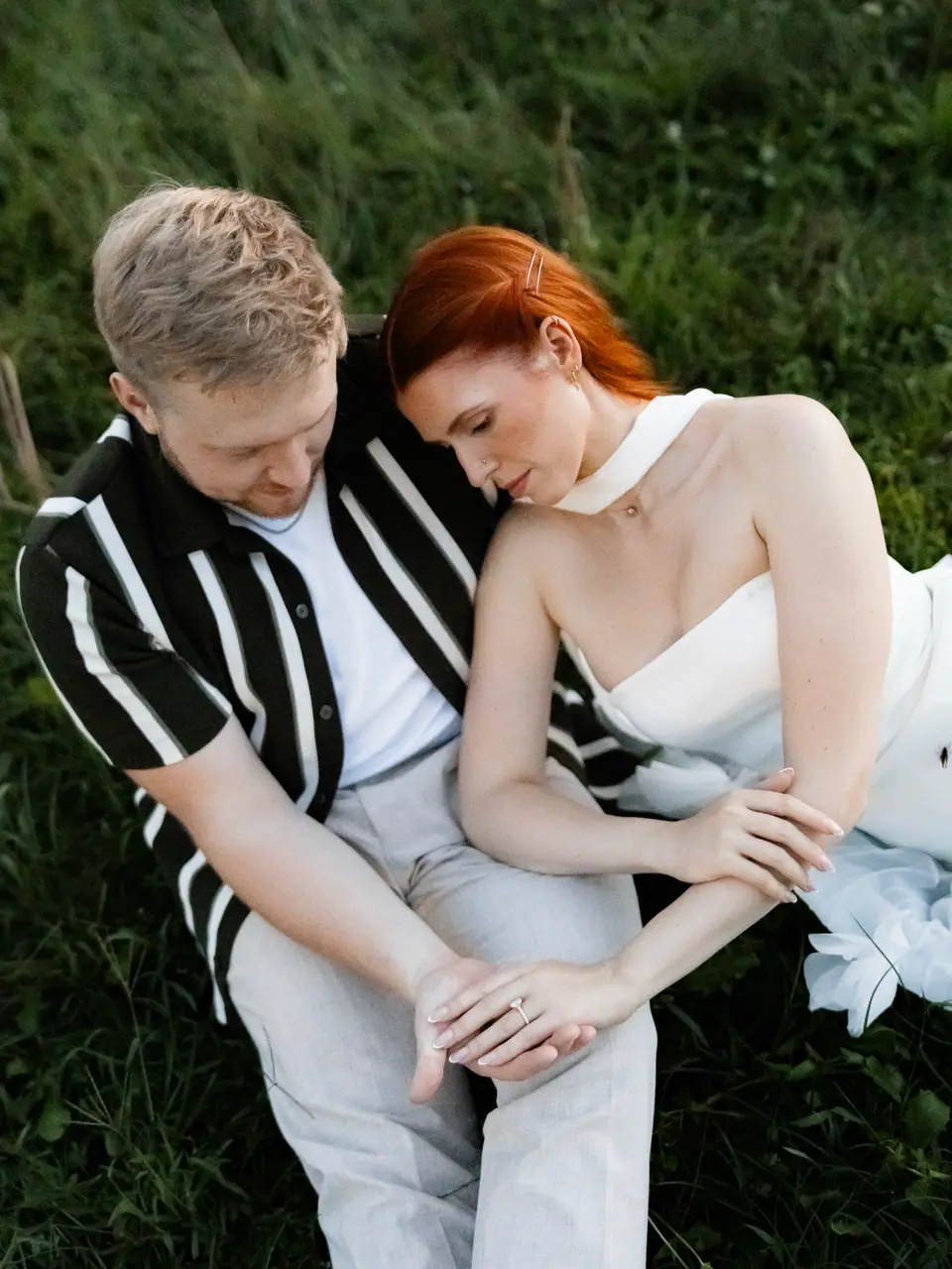 Kate and James sitting close in the grass, their hands together