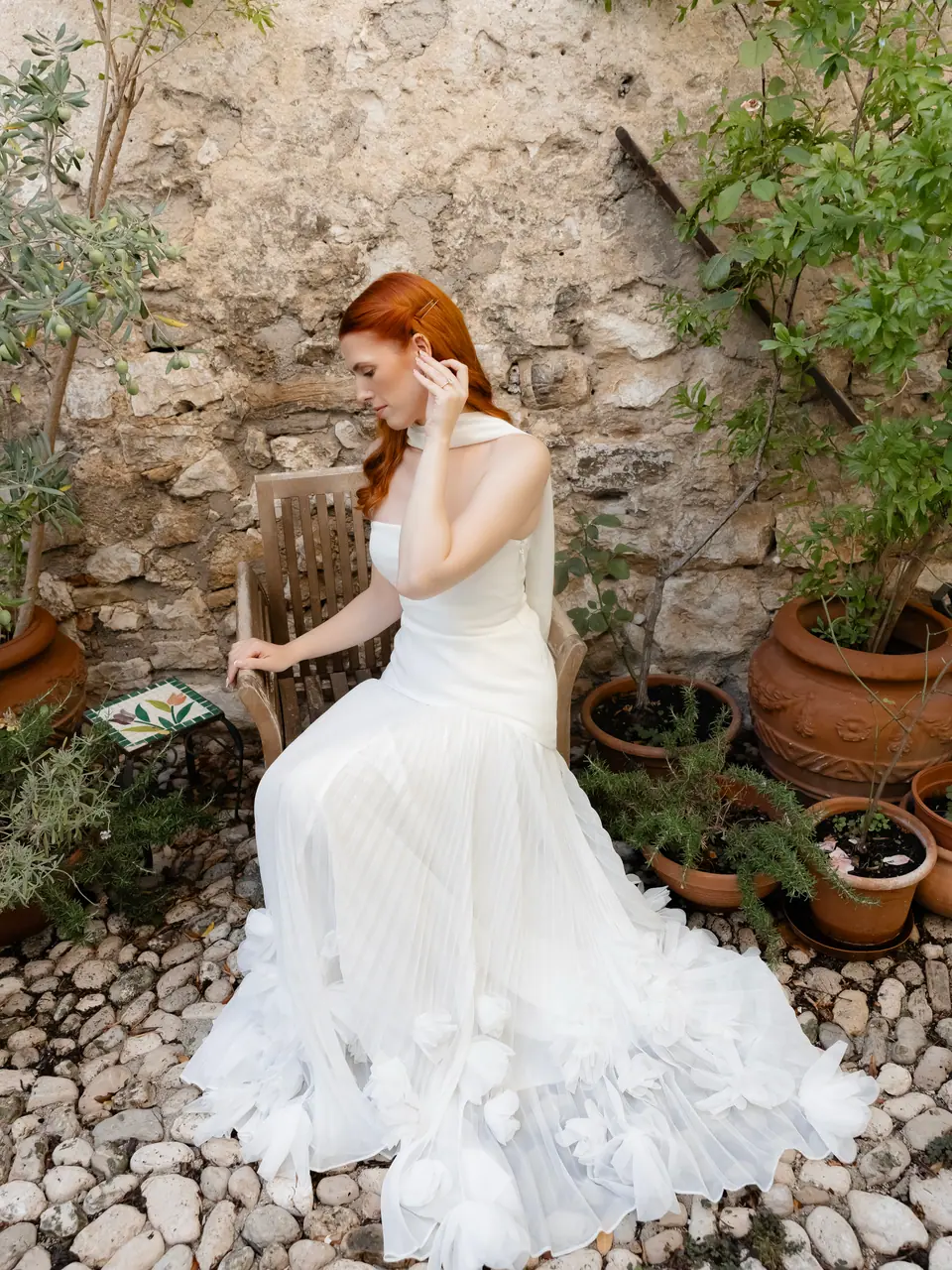 Kate sitting on a wooden chair in a stone courtyard, her dress spread over the cobbles