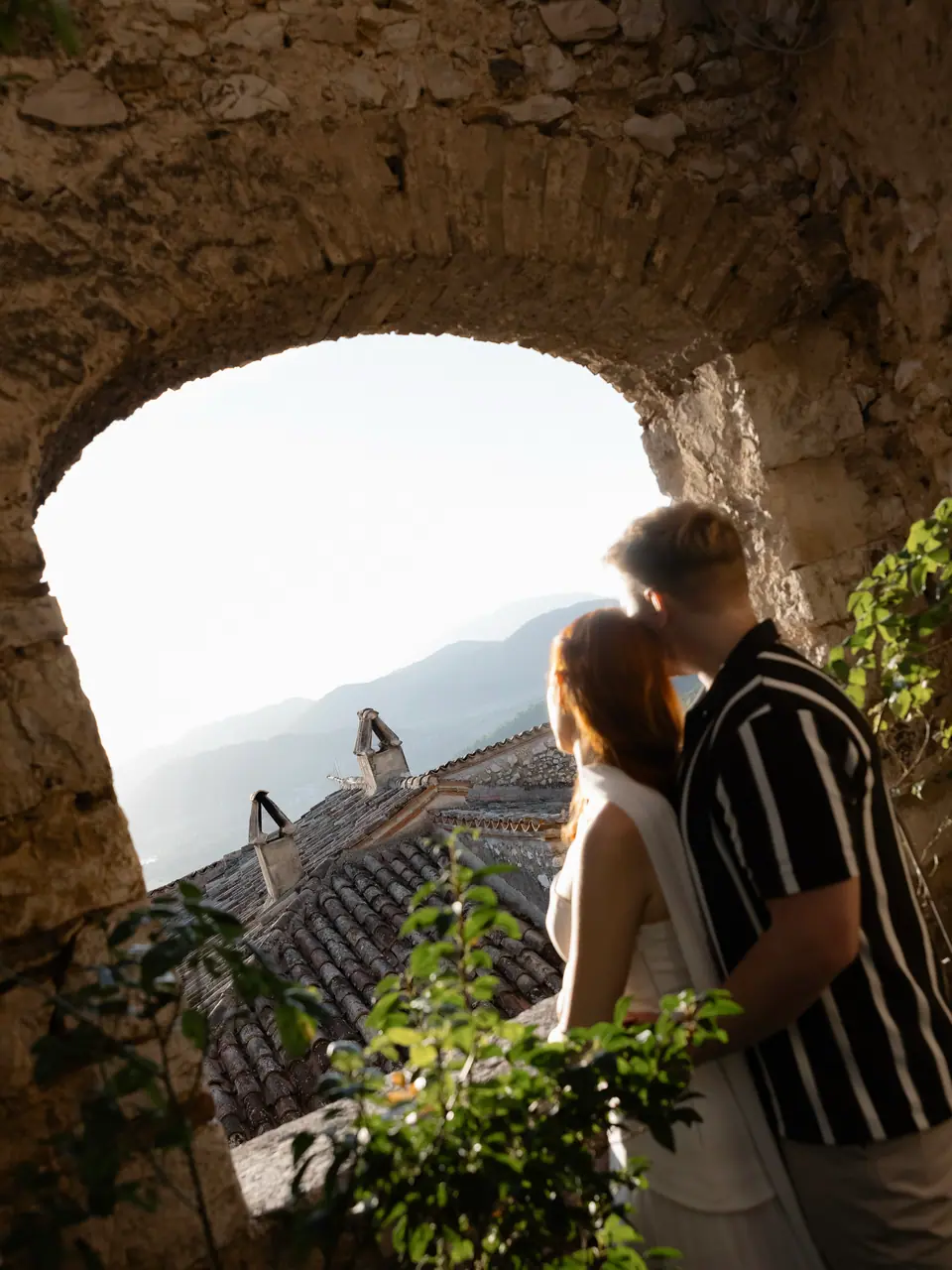 Kate and James sharing a kiss beneath a stone arch above the rooftops