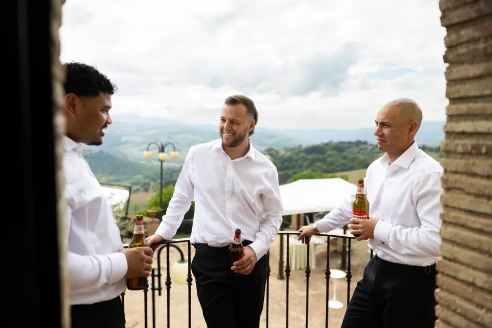 Rory sharing a drink with two groomsmen on a balcony above the Umbrian hills