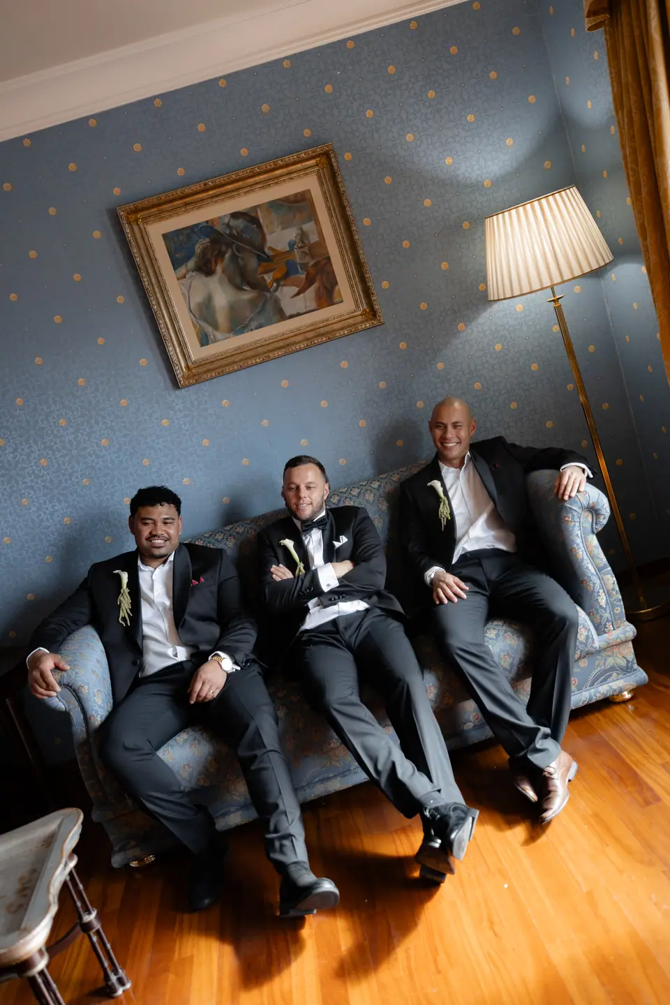 Rory and two groomsmen lounging on the blue sofa in their tuxedos