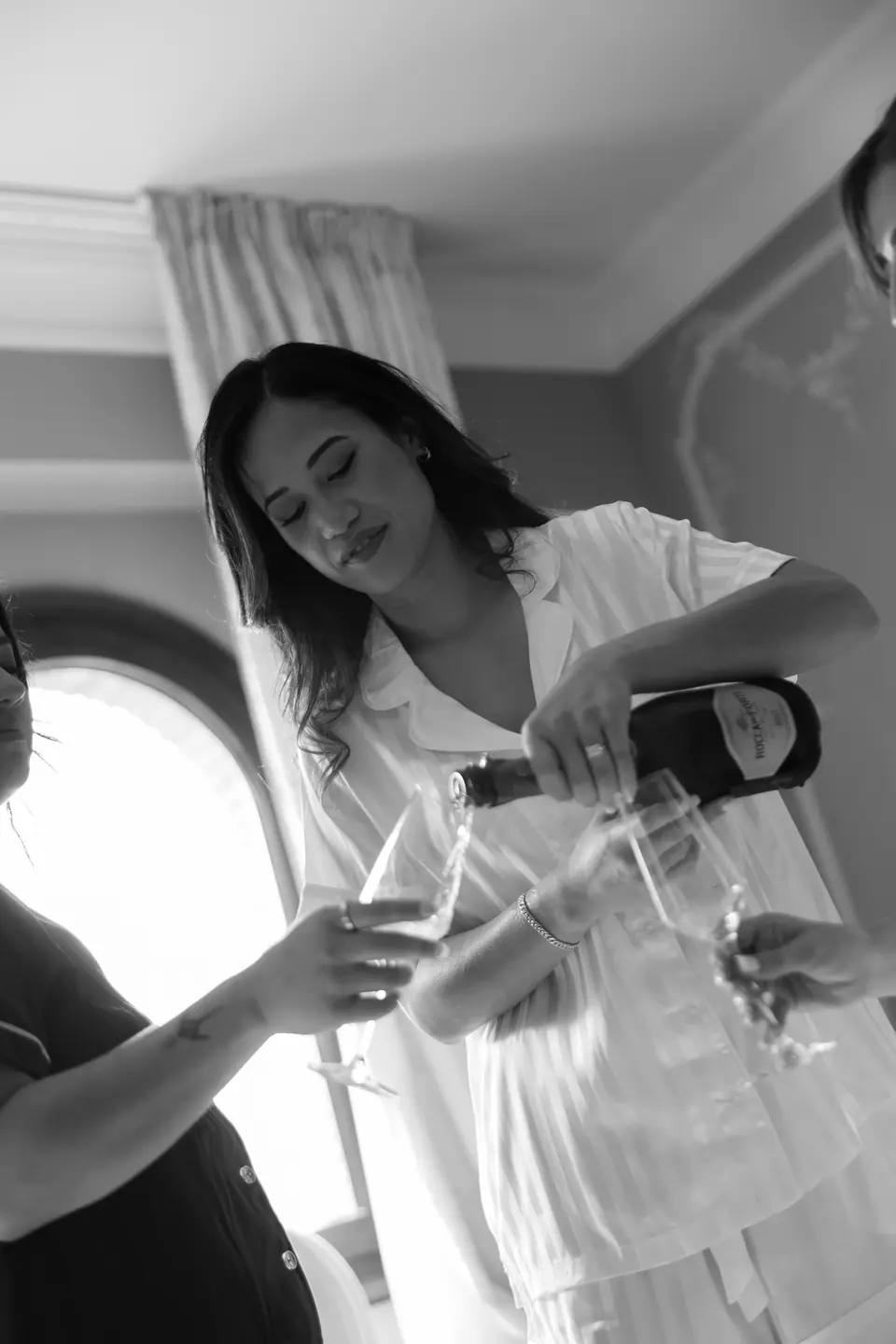 Black and white photograph of Sivitha pouring champagne in her robe