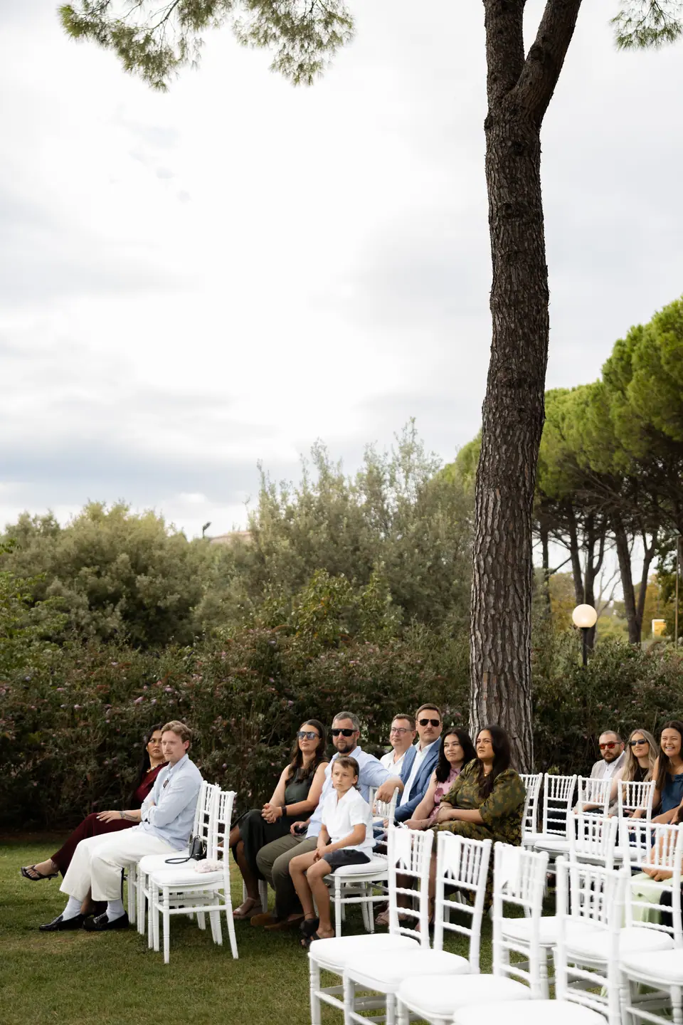 Guests seated on white chairs under the umbrella pines before the ceremony
