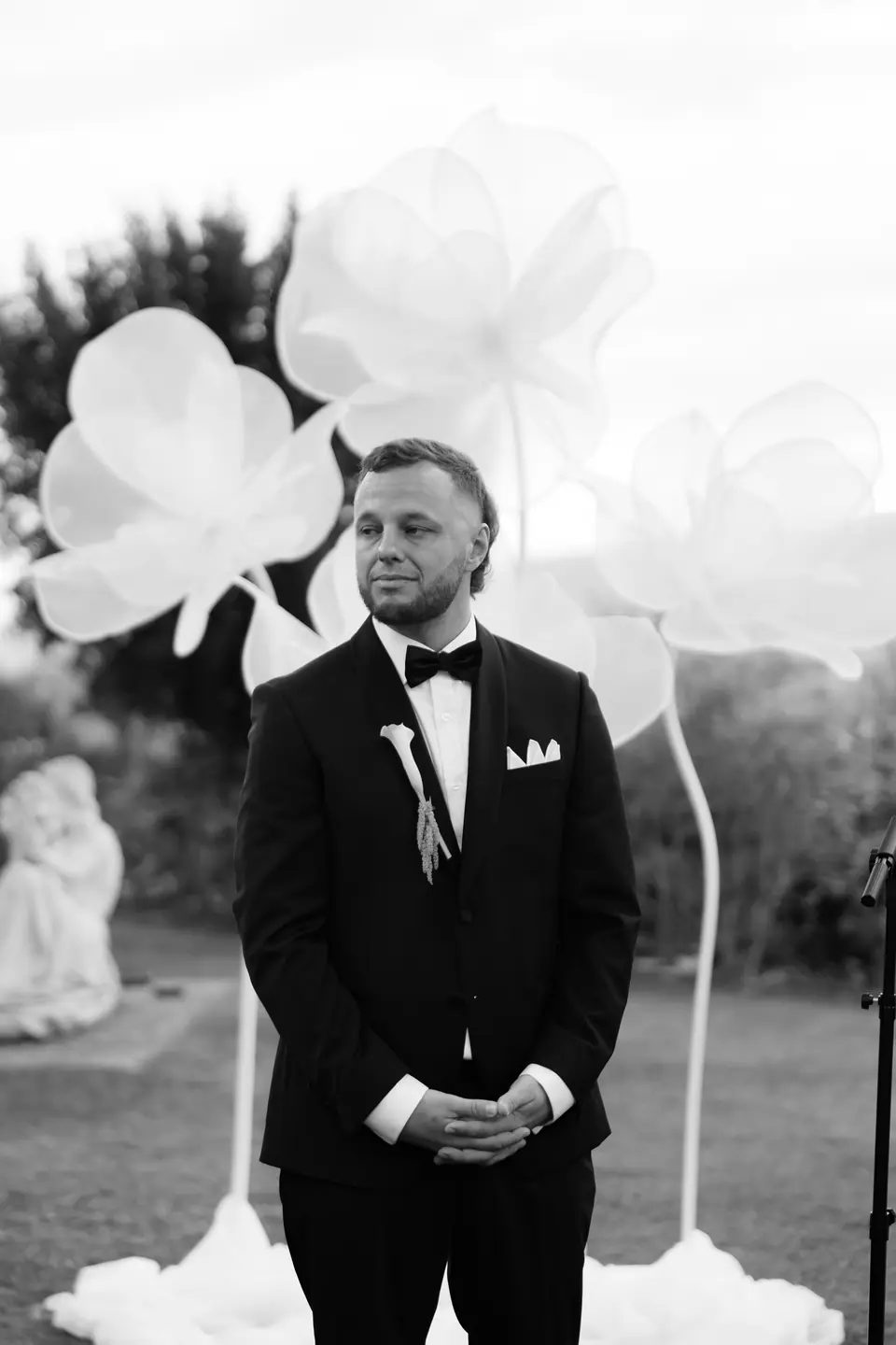 Black and white photograph of Rory waiting among giant white paper flowers