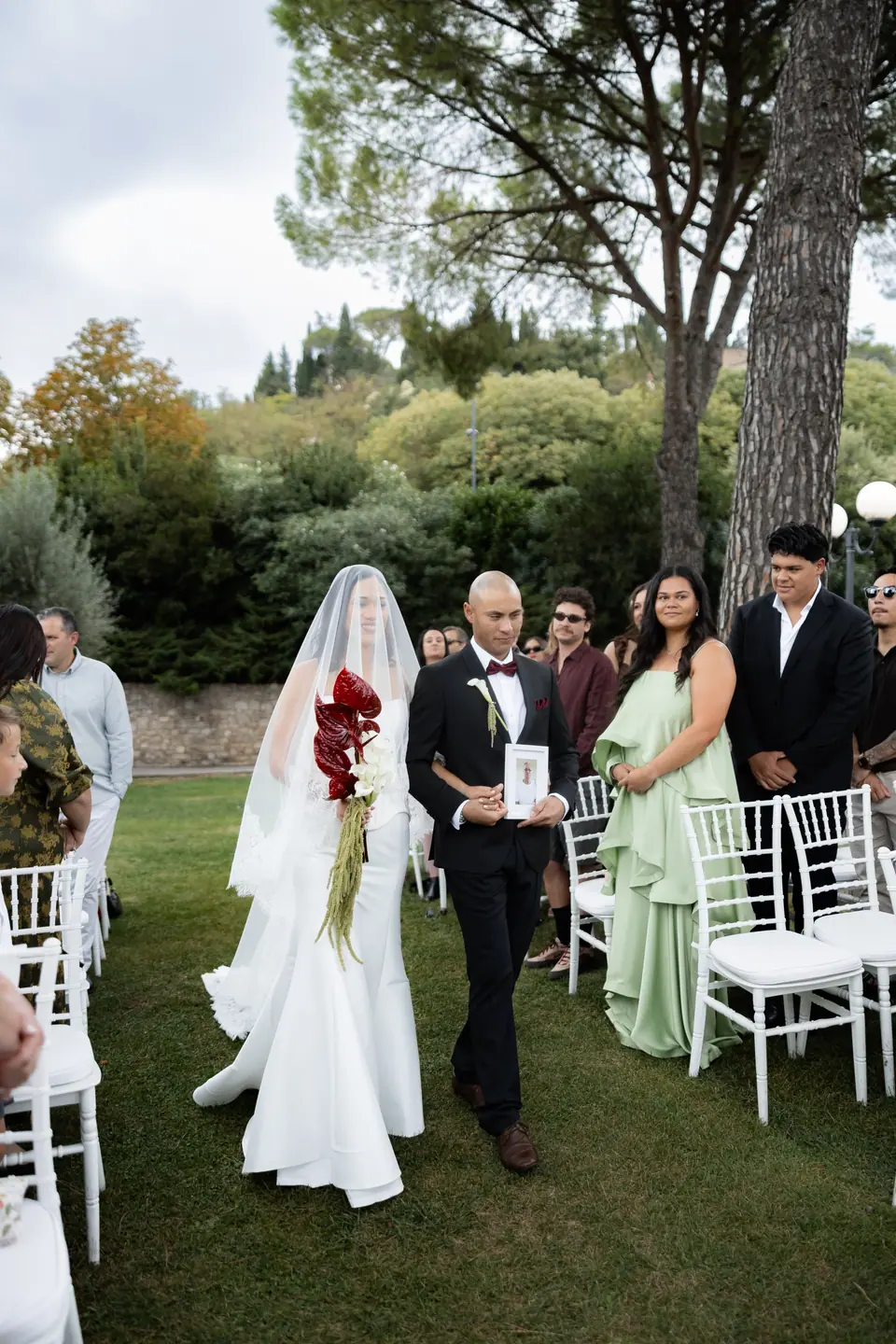 Sivitha walking down the aisle with a red bouquet on a man’s arm