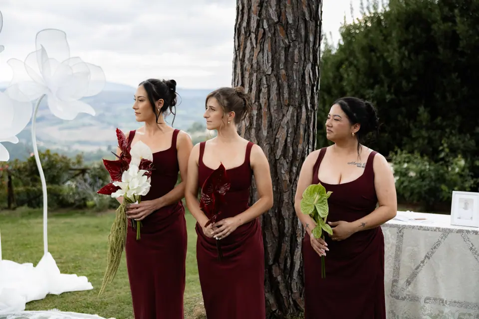 Three bridesmaids in deep red dresses holding red and white flowers