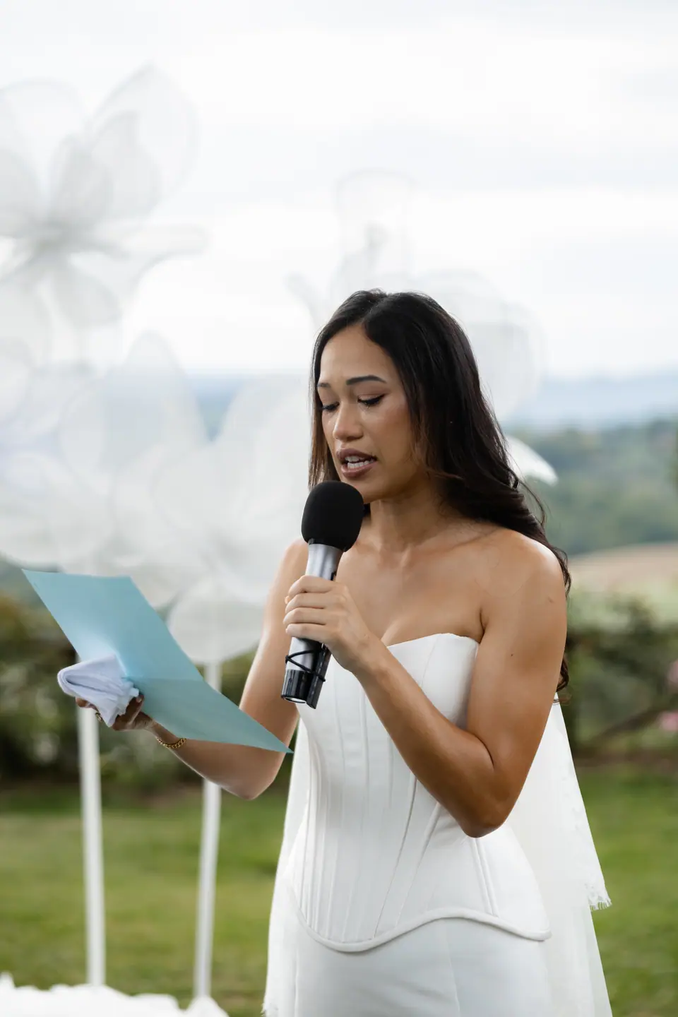 Sivitha reading her vows into a microphone among the paper flowers