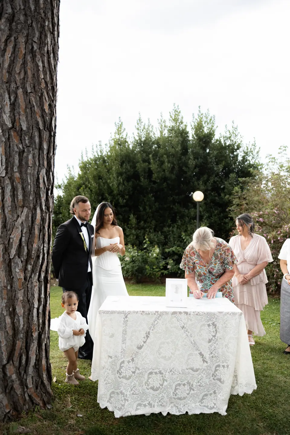 Signing the register at a lace-covered table beneath a pine