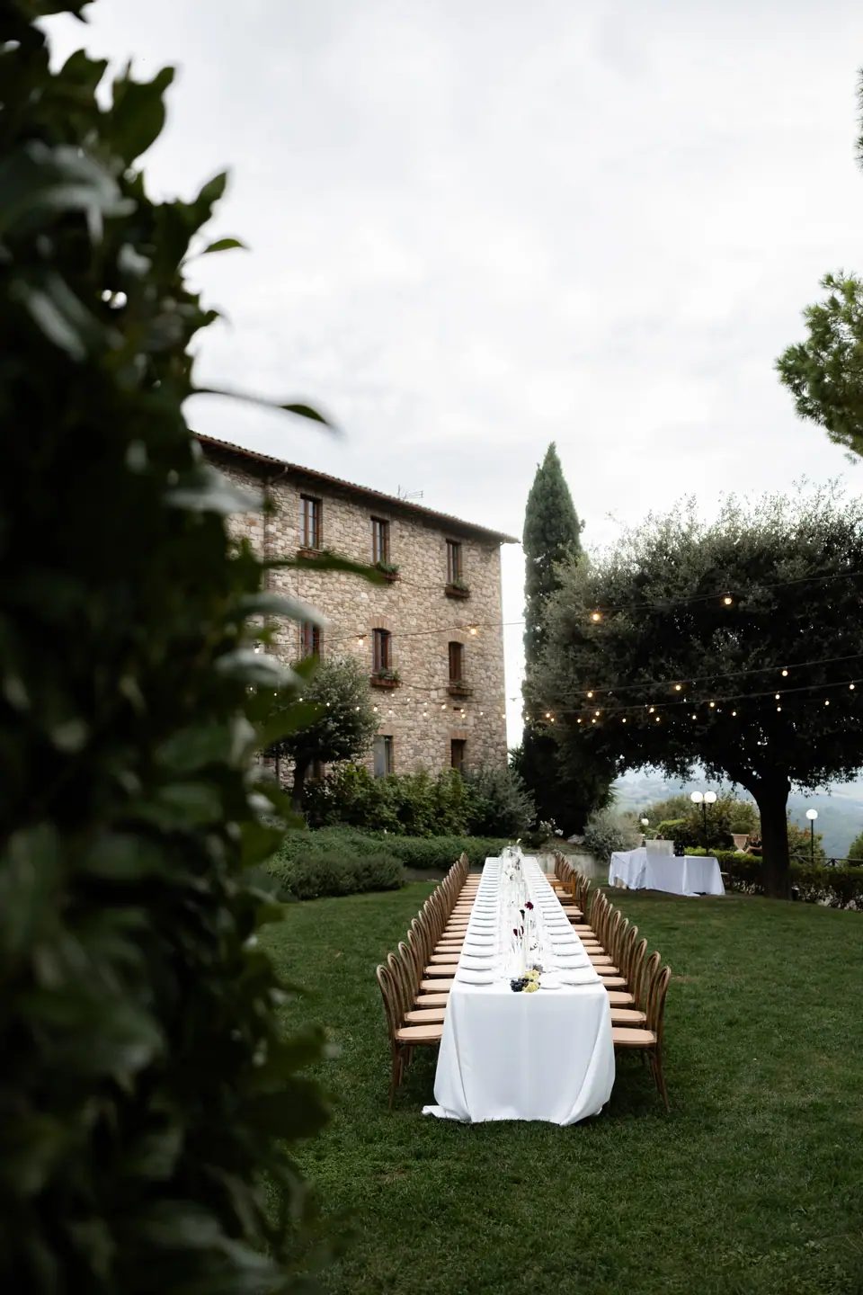 The long table on the lawn seen past a hedge, the stone monastery behind