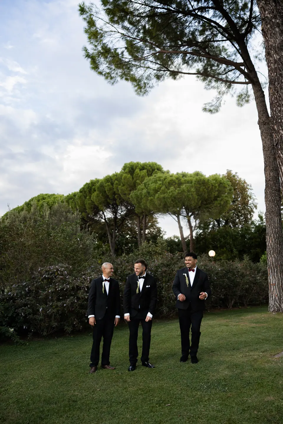 Rory and two groomsmen walking under the umbrella pines