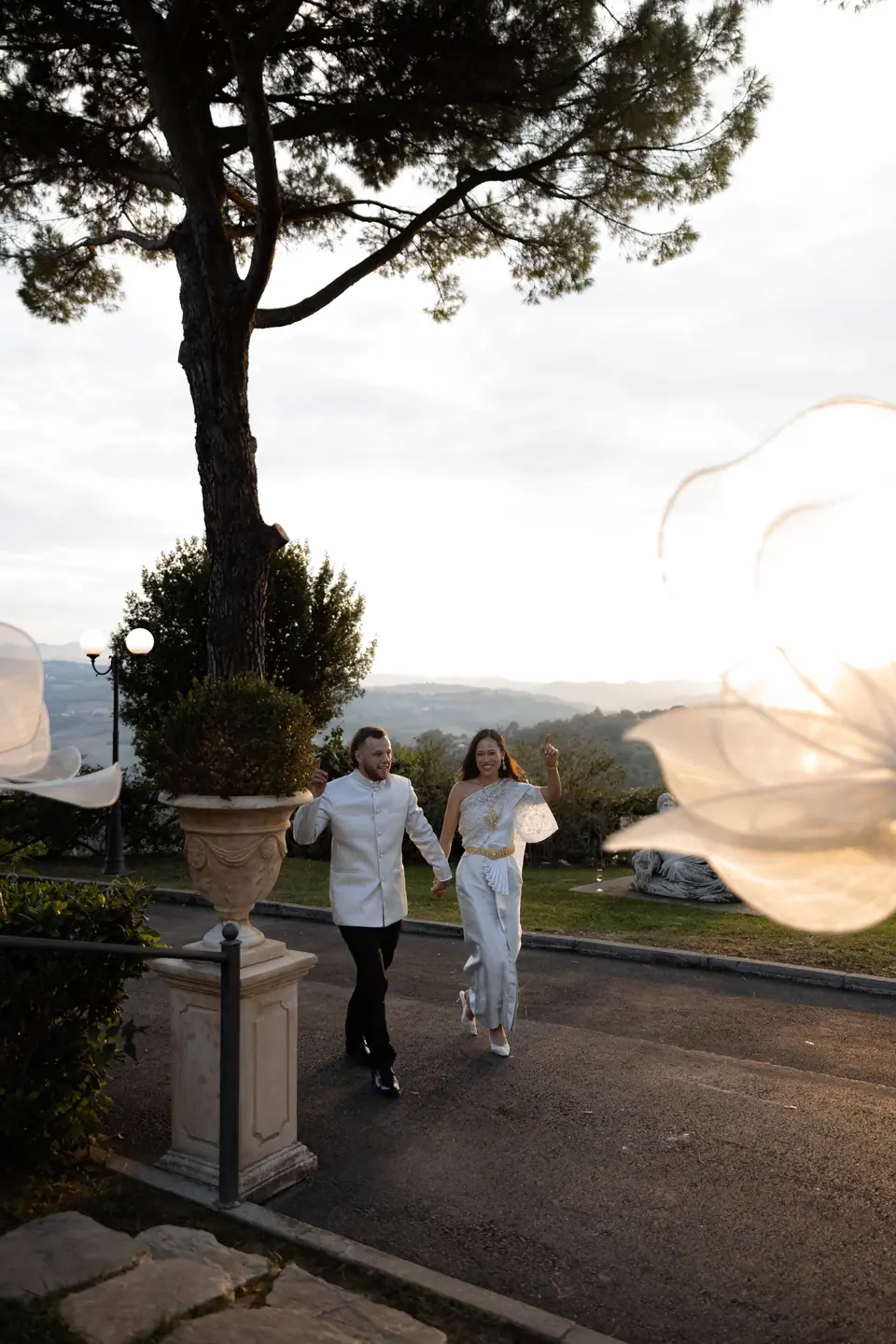 Sivitha and Rory in their evening outfits walking in past a stone urn