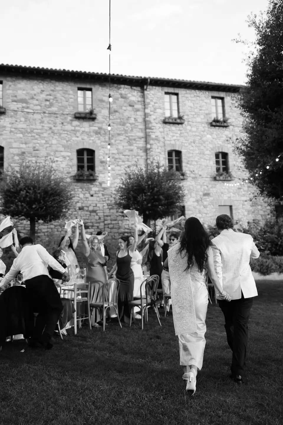 Black and white photograph of the couple walking towards cheering guests by the monastery wall