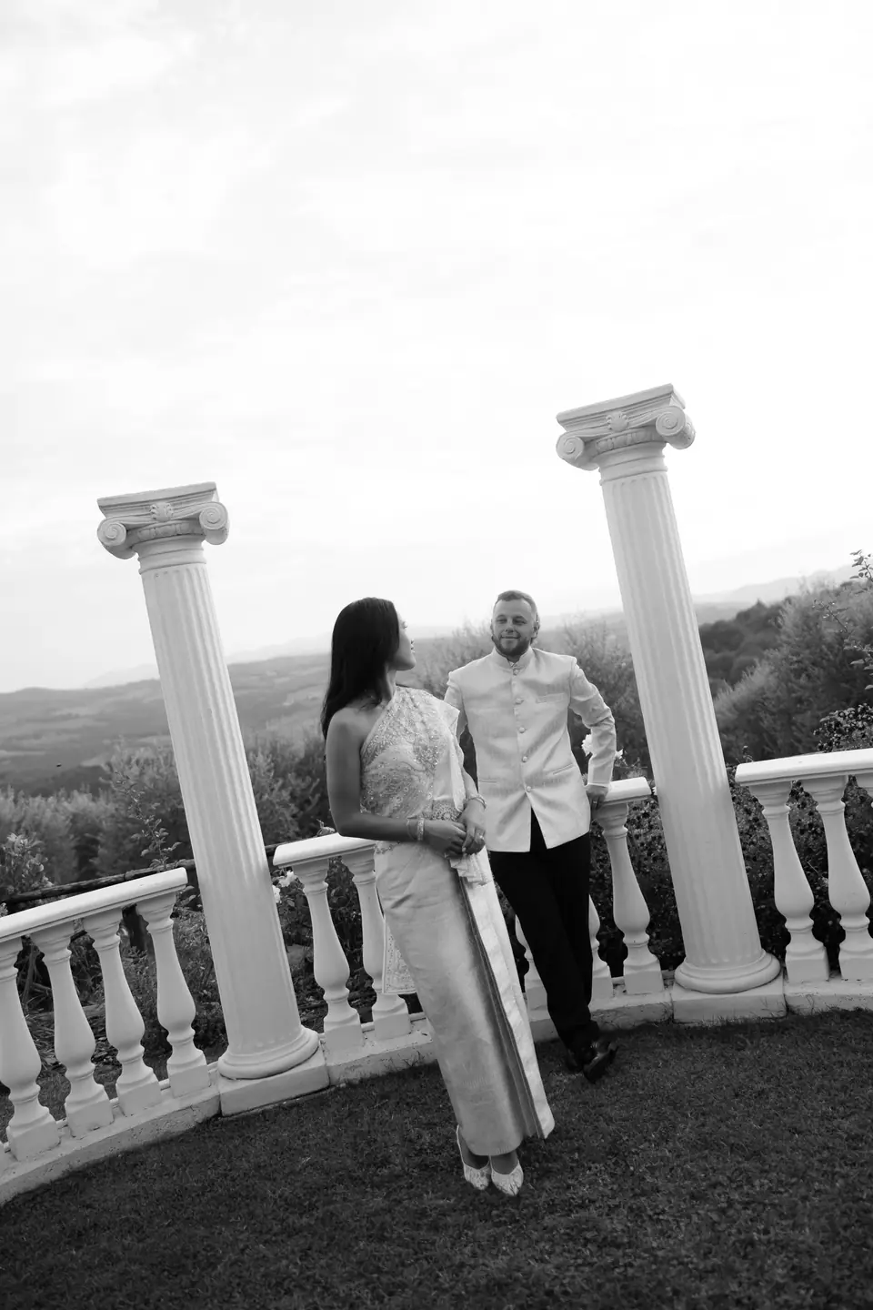 Black and white photograph of the couple between white columns on the balustraded terrace